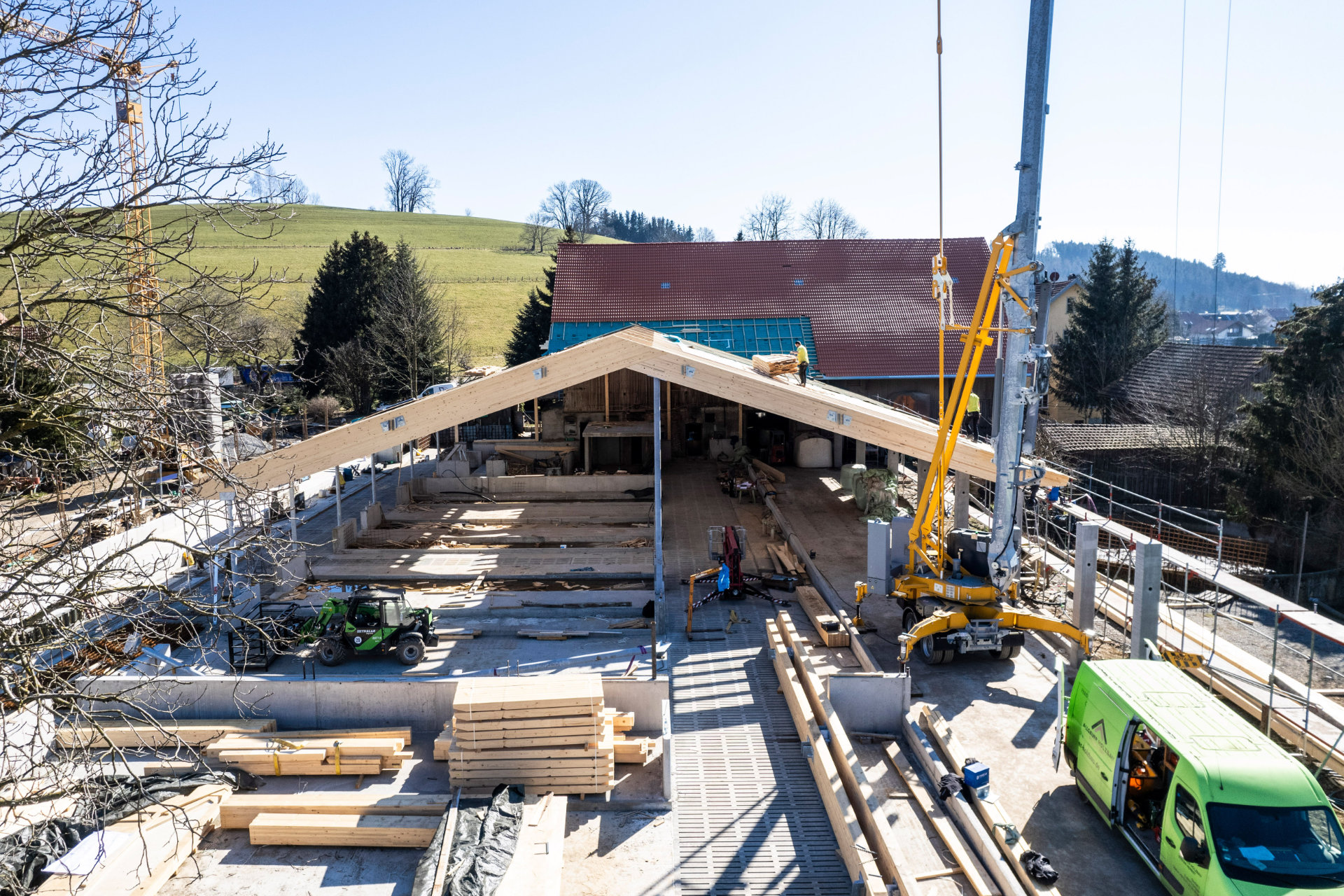 Baustelle eines Kuhstalls mit Handwerkern, Kran und Baumaterial