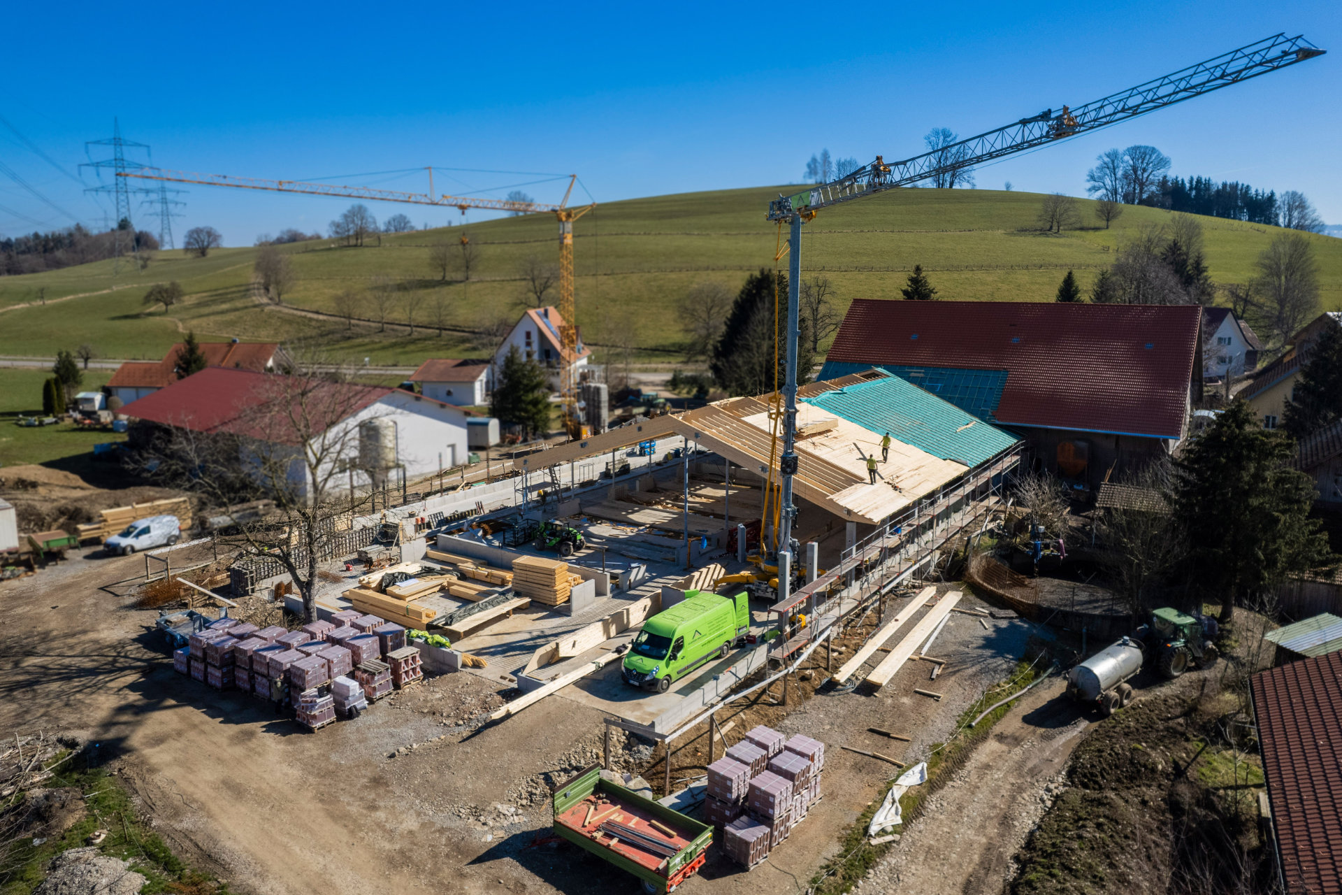 Baustelle des Kuhstalls in Wangen im Allgäu mit Kran, im Vordergrund ein Firmenfahrzeug von Allgäuer Holzbau