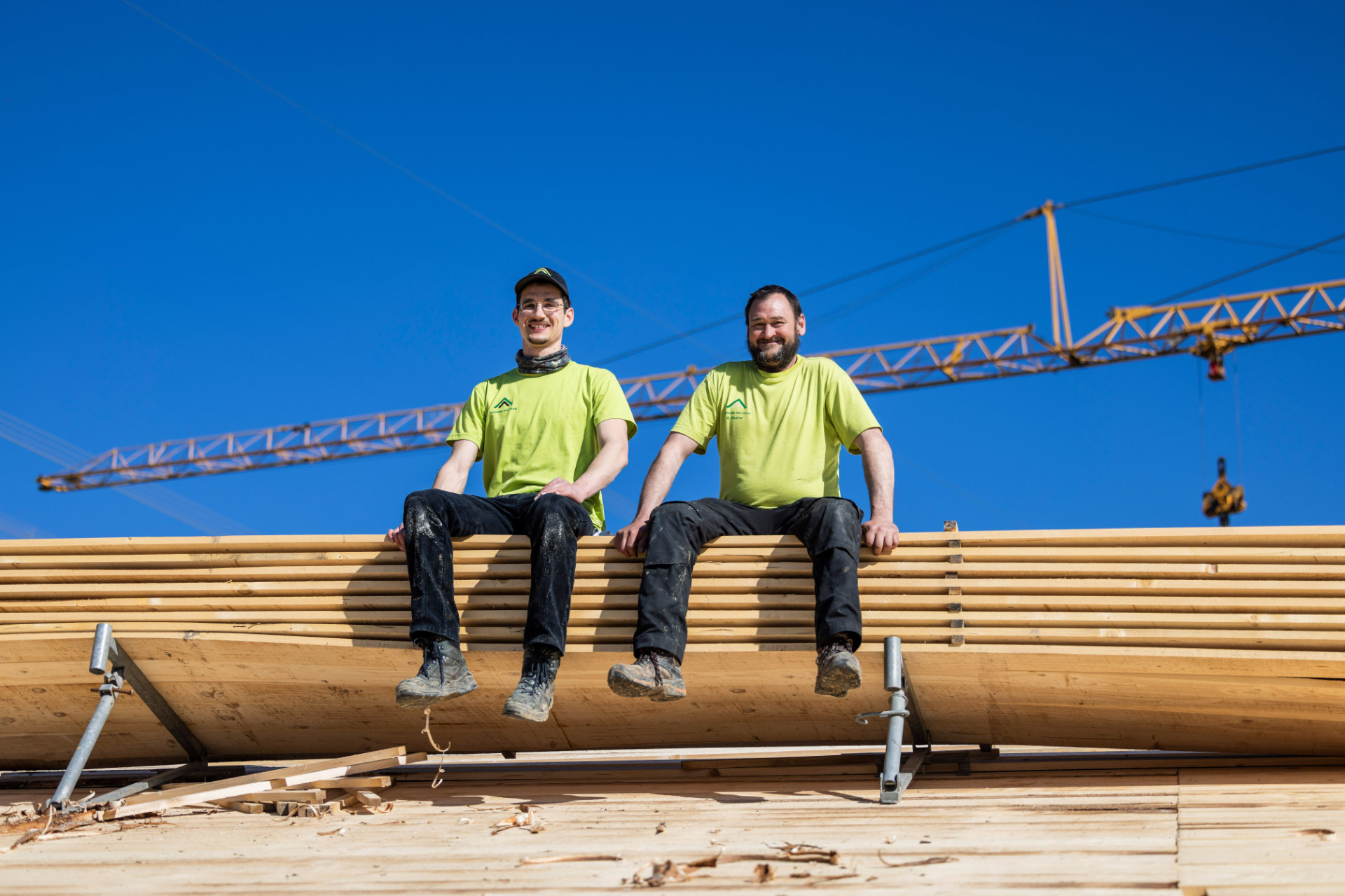 Zwei Mitarbeiter von Allgäuer Holzbau sitzen auf dem Dach eines Kuhstalls