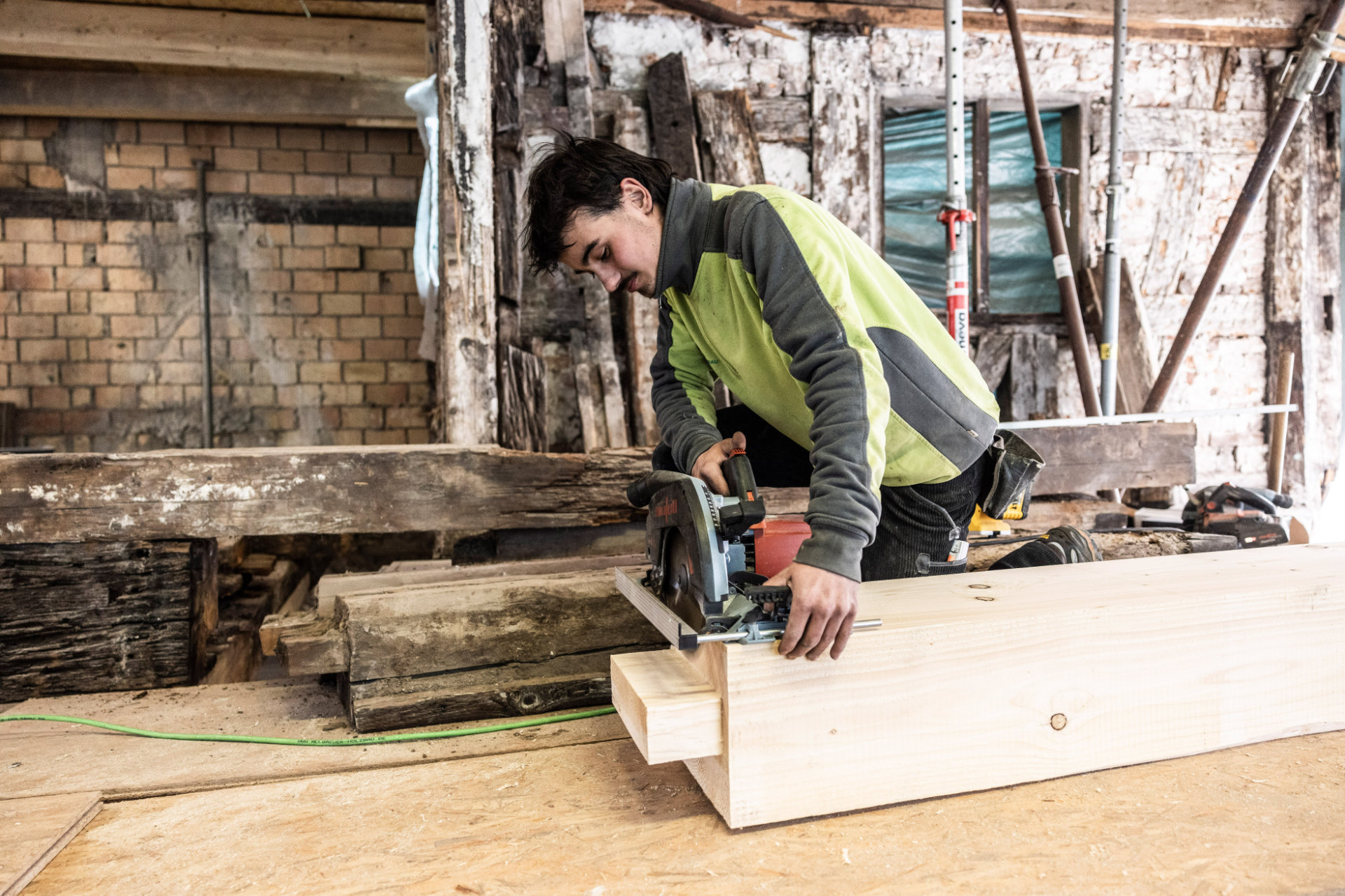Ein Mitarbeiter von Allgäuer Holzbau sägt einen Holzbalken mit einer Tauchsäge ab