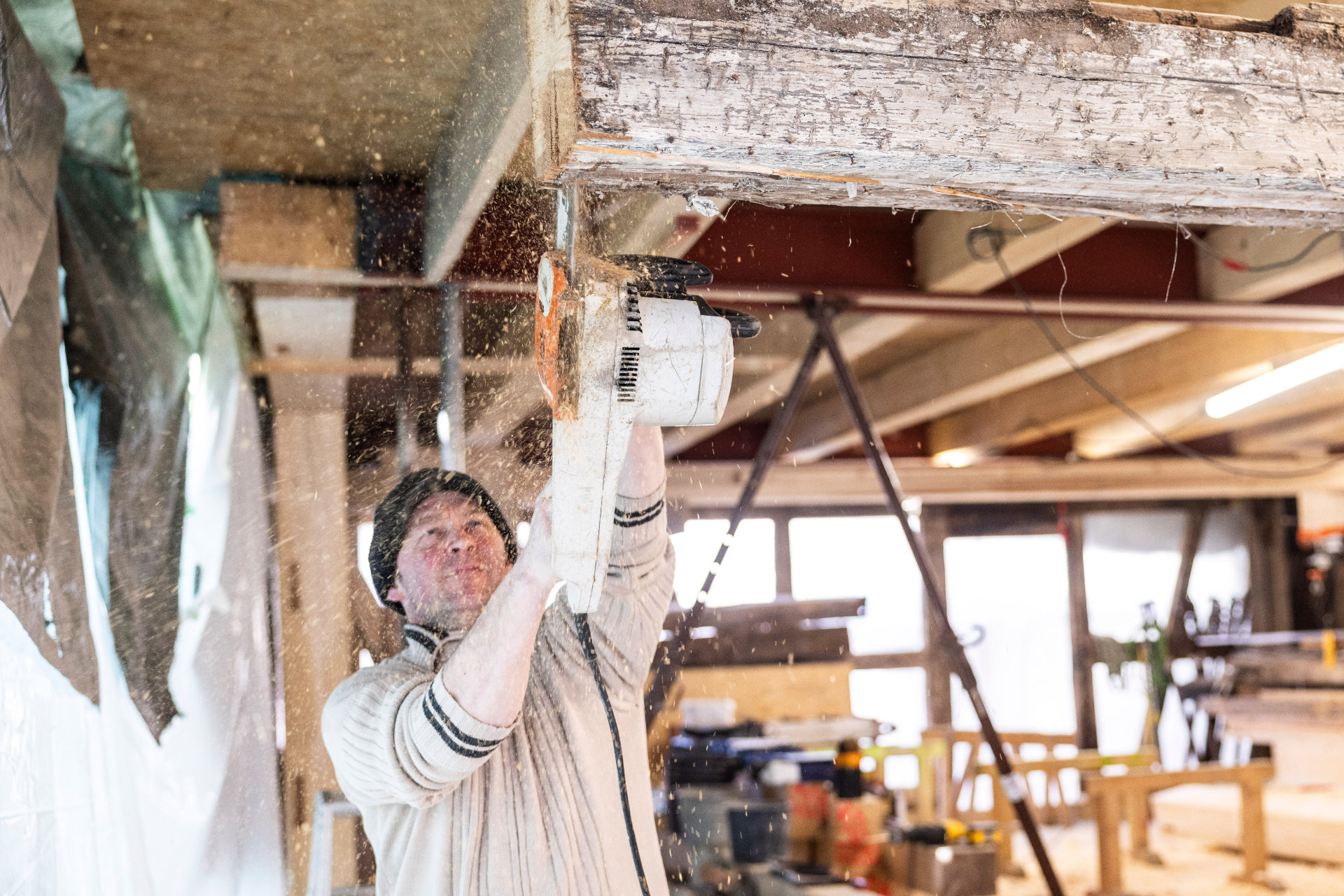 Ein Mitarbeiter von Allgäuer Holzbau sägt einen Holzbalken über Kopf mit einer Kettensäge
