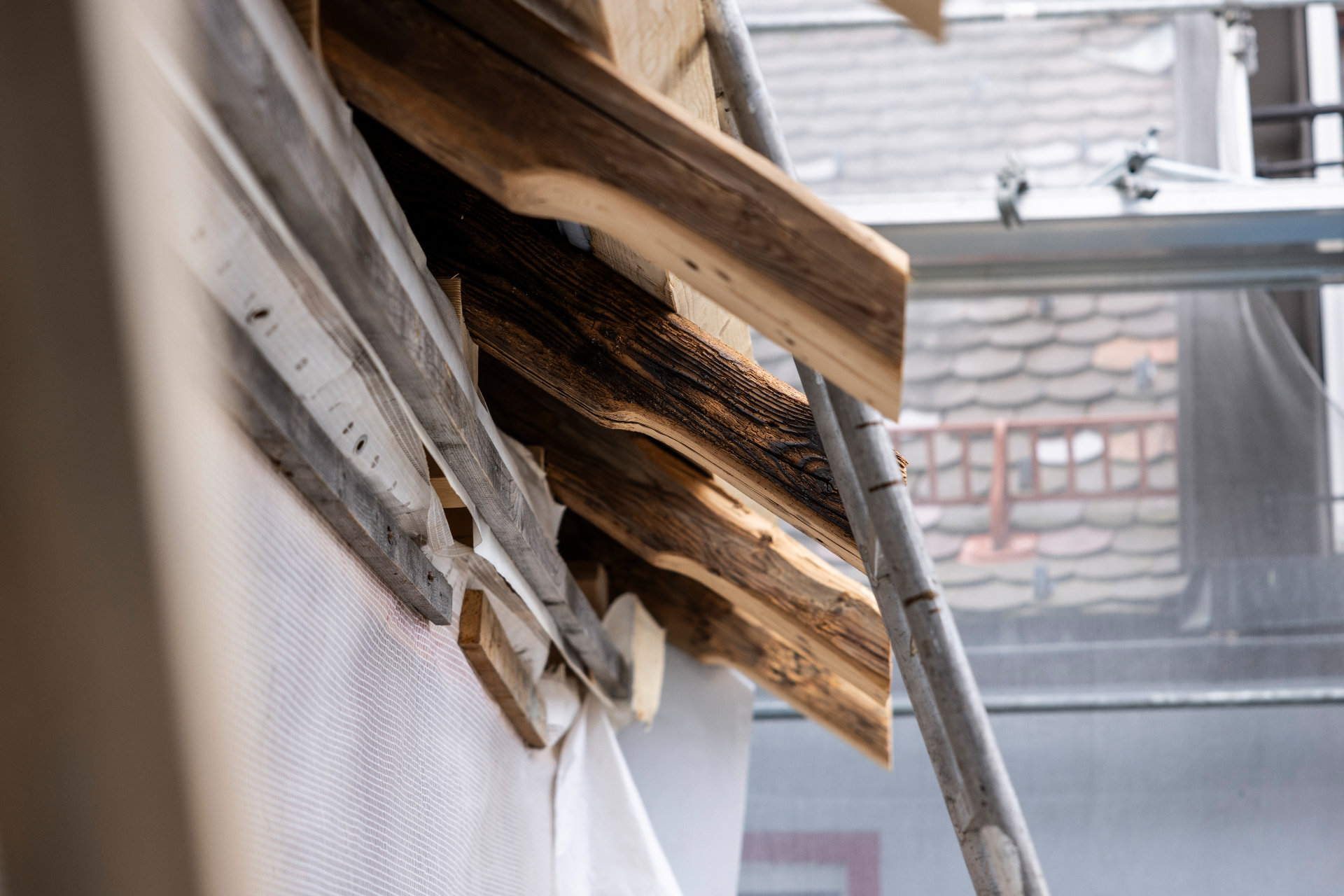 Antike Dachbalken Antike Dachbalken schauen unter einem Dach hervor, daneben ein Baugerüst aus Metall.