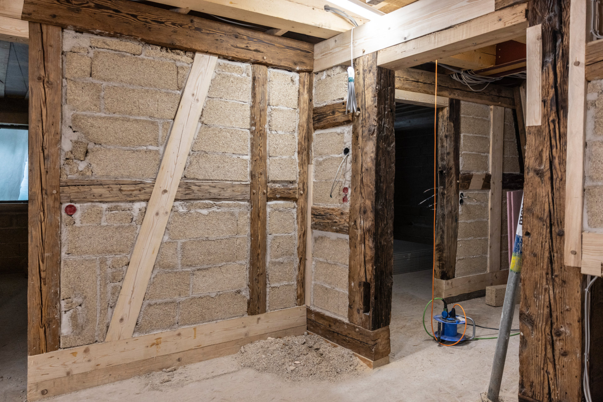 Sanierung einer Fachwerkwand m Innenraum Innenansicht einer Fachwerkwand mit Lehmziegel-Ausfachung während der Sanierung; sichtbare Holzbalken und moderne Elektroinstallation.