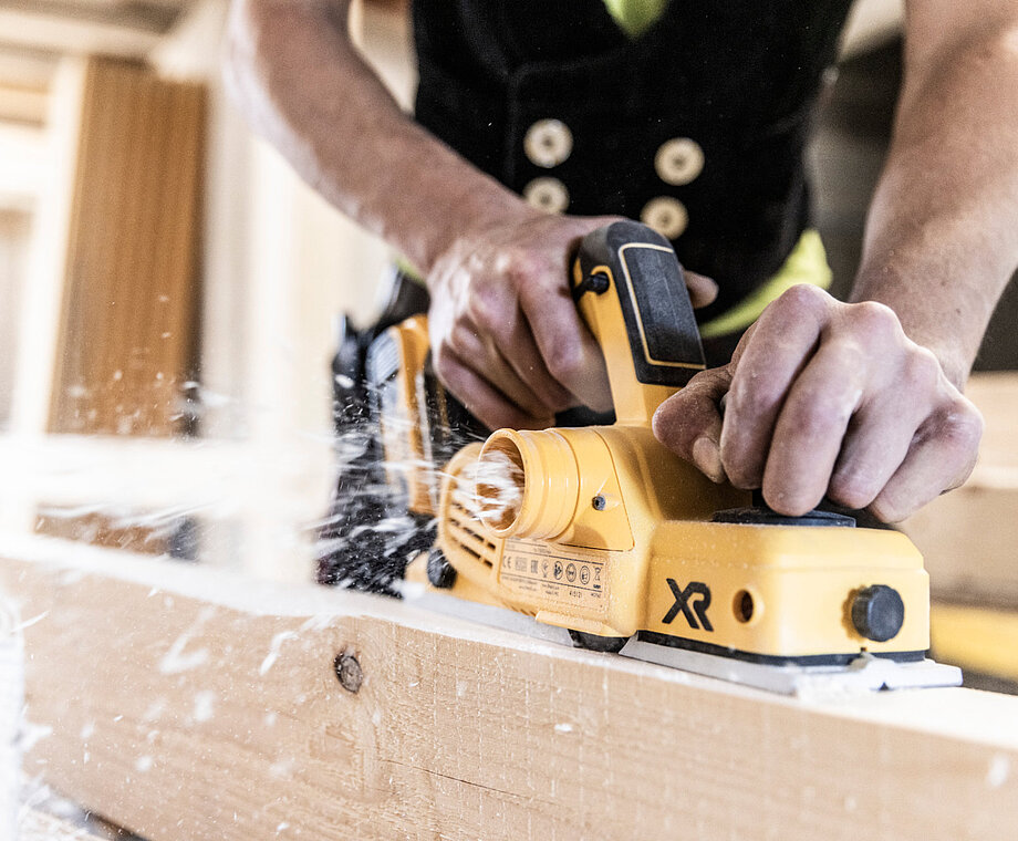 Ein Mann bearbeitet einen Holzbalken mit einer Schleifmaschine