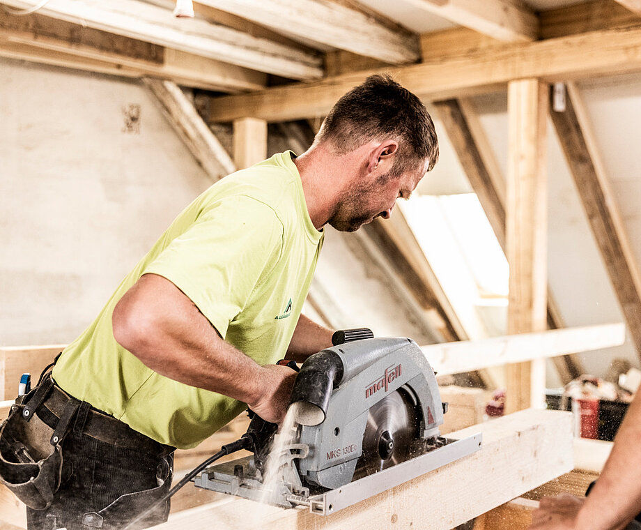 Ein Mitarbeiter von Allgäuer Holzbau sägt einen Balken mit einer Kreissäge