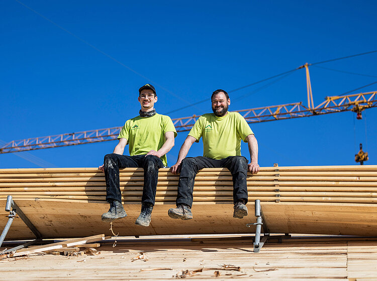 Auf dem Dach Zwei Mitarbeiter von Allgäuer Holzbau sitzen auf dem Dach eines Kuhstalls