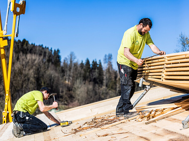 Holzarbeiten auf dem Dach Zwei Mitarbeiter von Allgäuer Holzbau führen Holzarbeiten auf einem Dach aus
