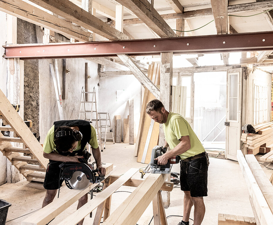 Mann bearbeitetet einen Holzbalken auf einer Baustelle