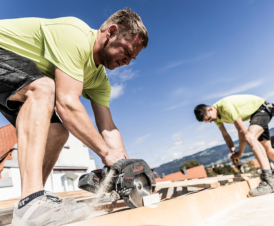 Zwei Männer sägen Holz auf eine Hausdach
